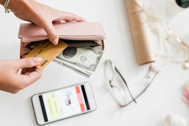 hands-young-woman-holding-nude-beige-leather-wallet-with-dollar-bills-plastic-card-smartphone-eyeglasses-desk_274679-2740