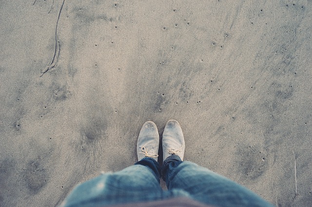 Mužské nohy v rifliach a sivých topánkach na piesku.jpg